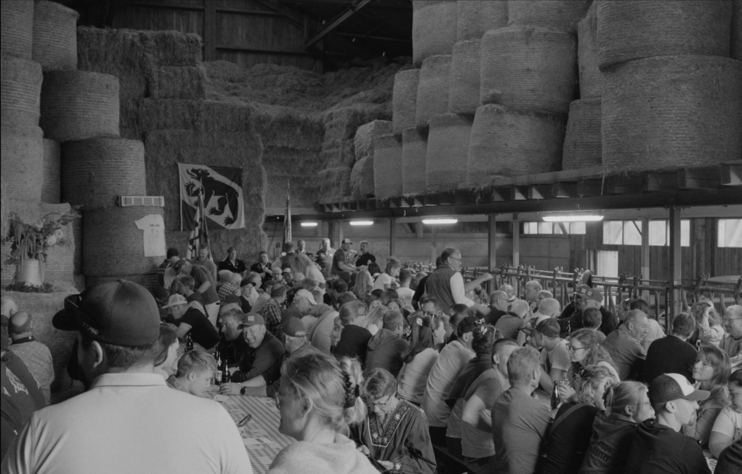 Une photo en noir et blanc d'un groupe d'environ 50 villageois réunis dans une grande. Drapeau bernois accroché en arrière plan.